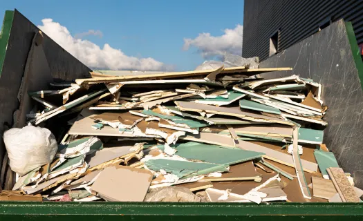 Open green roll-off dumpster loaded with construction debris and scrap metal for hauling in Dallas