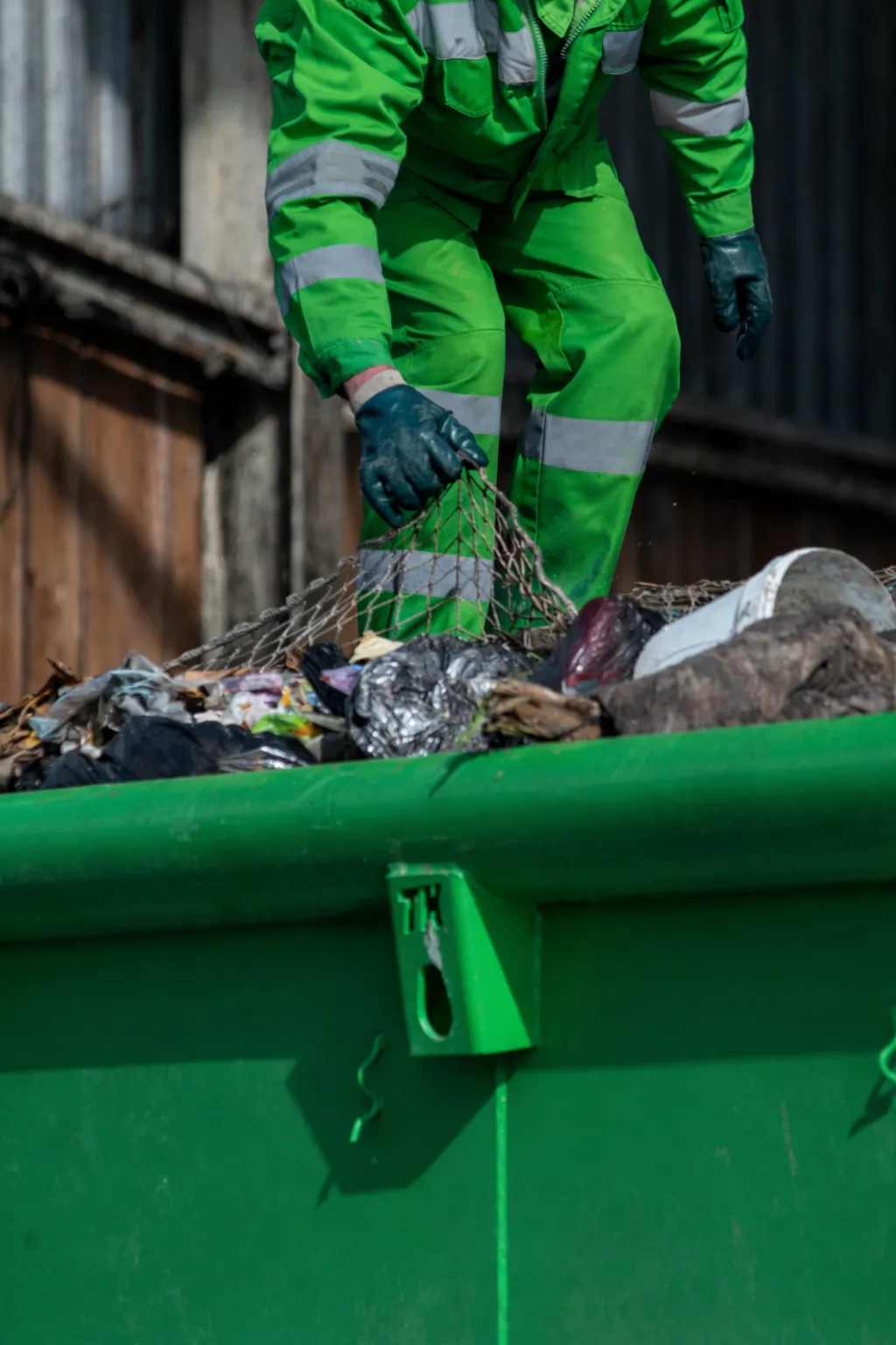 Professional waste handling by Dump Pro Dallas crew using safety gear and green roll-off dumpster